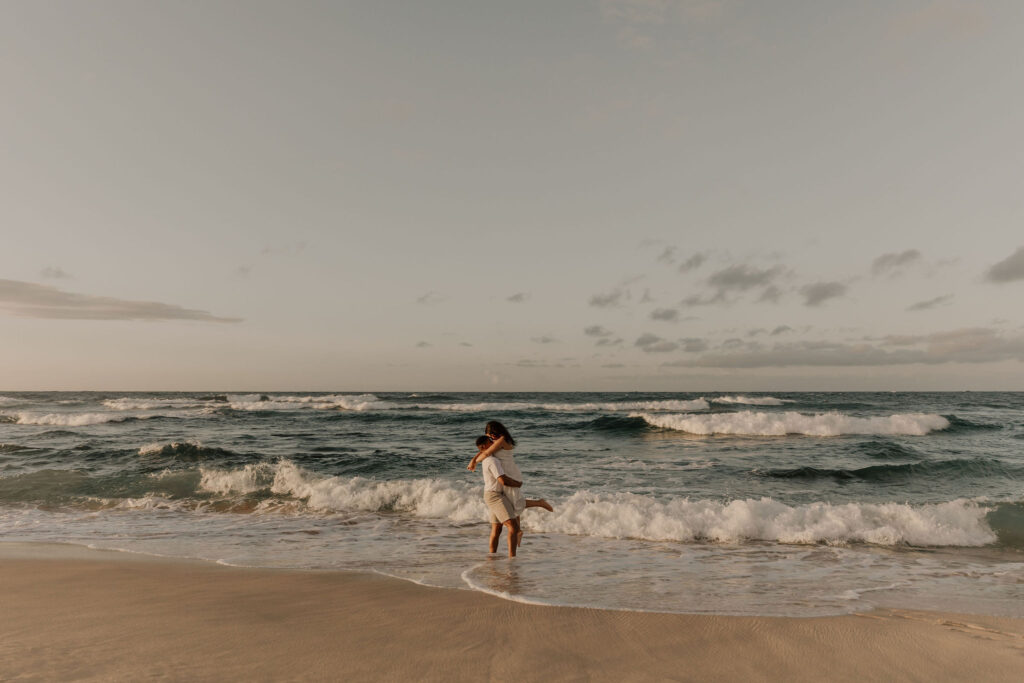 couple kissing in the waves on the beach at sunrise in Oahu, Hawaii