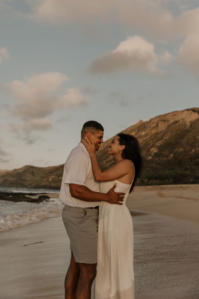 couple kissing on the beach in Oahu, Hawaii with mountains in background