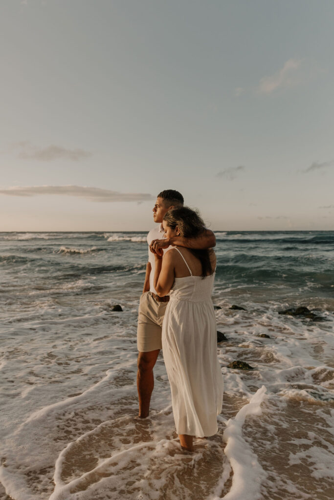 couple in the water admiring the sunrise on the beach at sunrise in Oahu, Hawaii