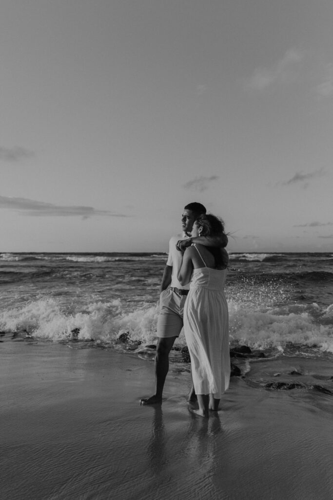 Couple standing in the water watching the sunrise on a beach in Oahu, Hawaii