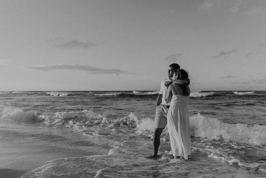 Couple standing in the water watching the sunrise on a beach in Oahu, Hawaii