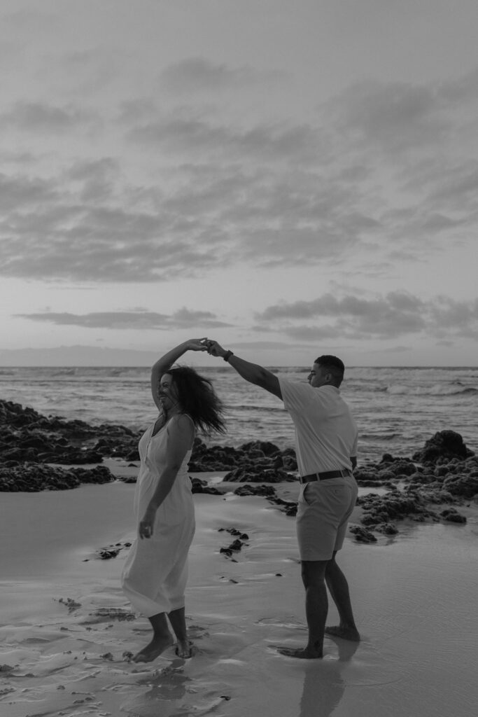Black and white of couple dancing between lava rock on Oahu, Hawaii beach