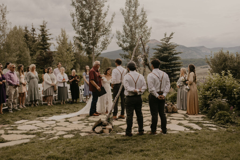 Father giving daughter away under wildflower arch in Rocky Mountains