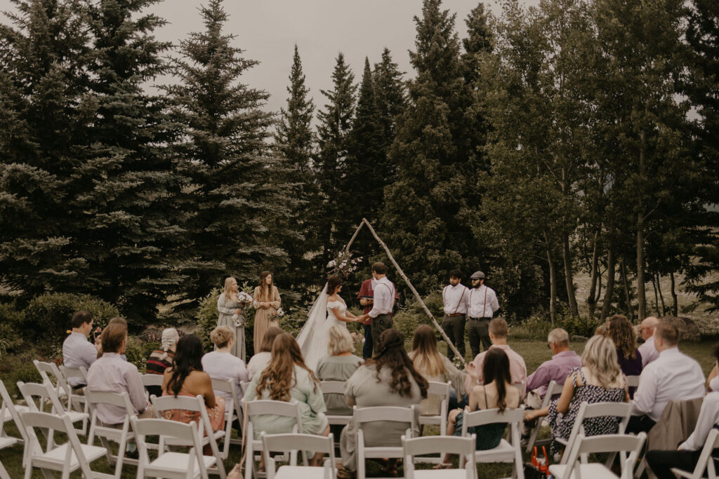 Couple exchanging vows under wildflower arch surrounded by family in Rocky Mountains