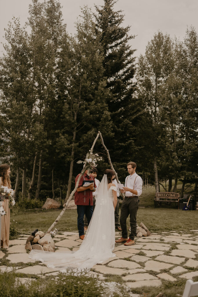 Couple exchanging vows under wildflower wedding arch in Rocky Mountains