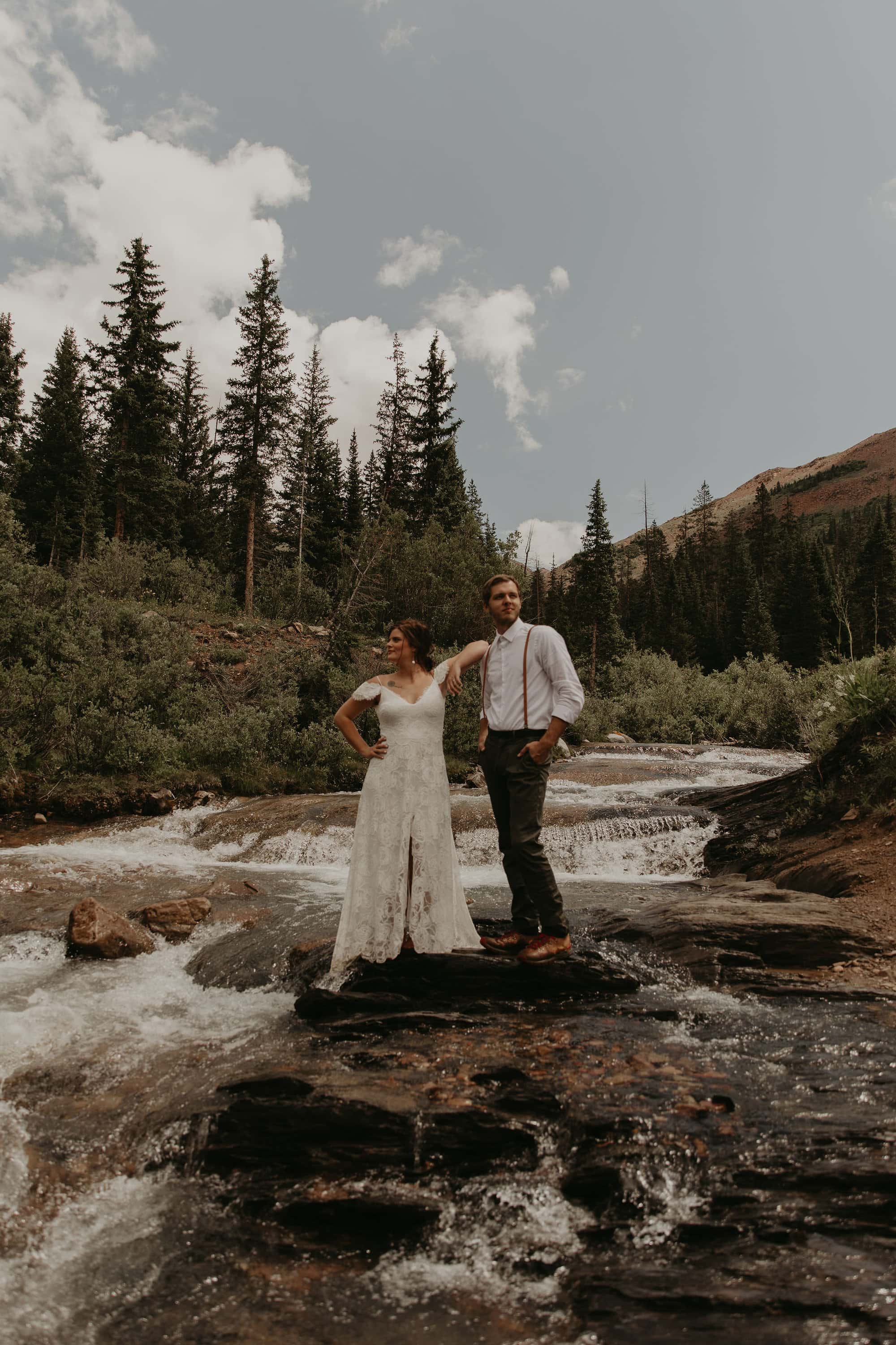 Couple walking barefoot through a river in their wedding clothes