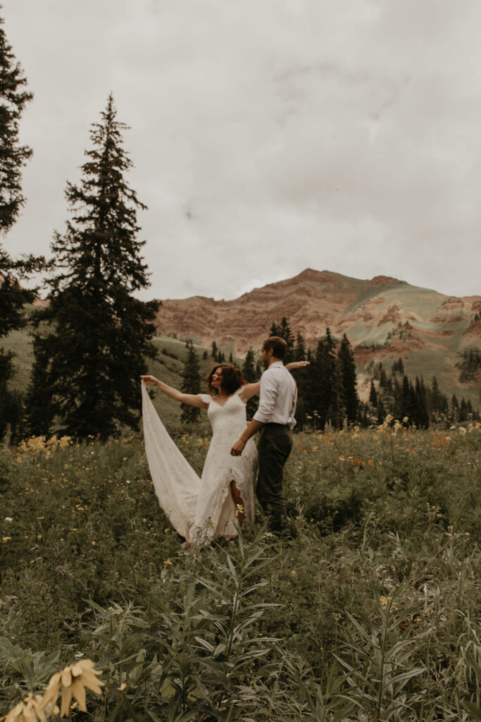 Wedding couple dancing in wildflower fields at the base of mountains