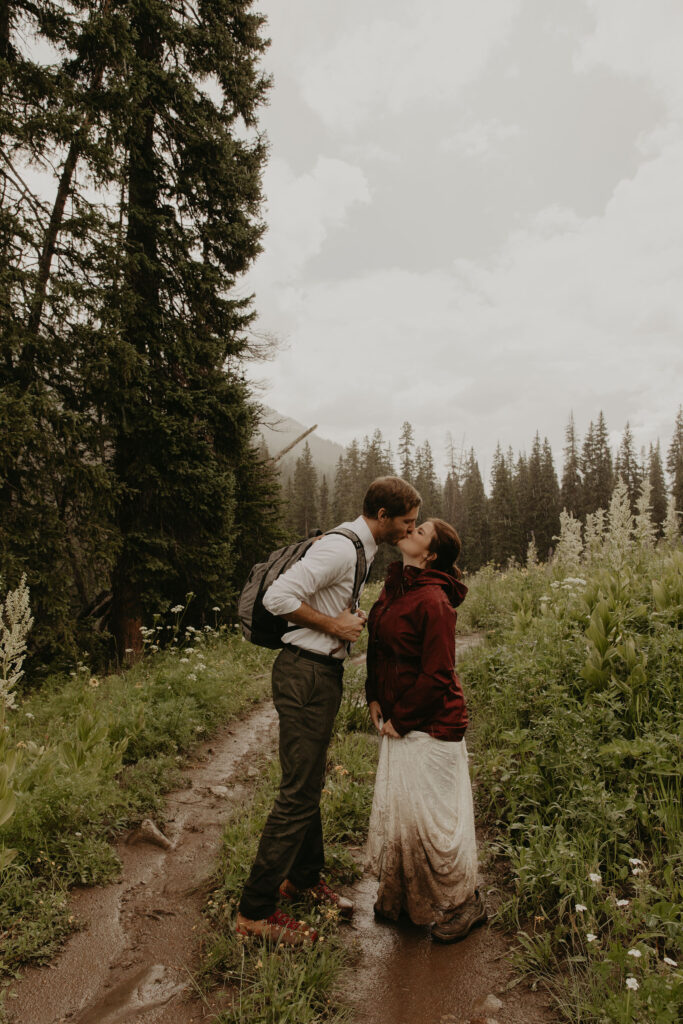 Couple kissing on a hiking trail with bride's wedding dress covered in mud