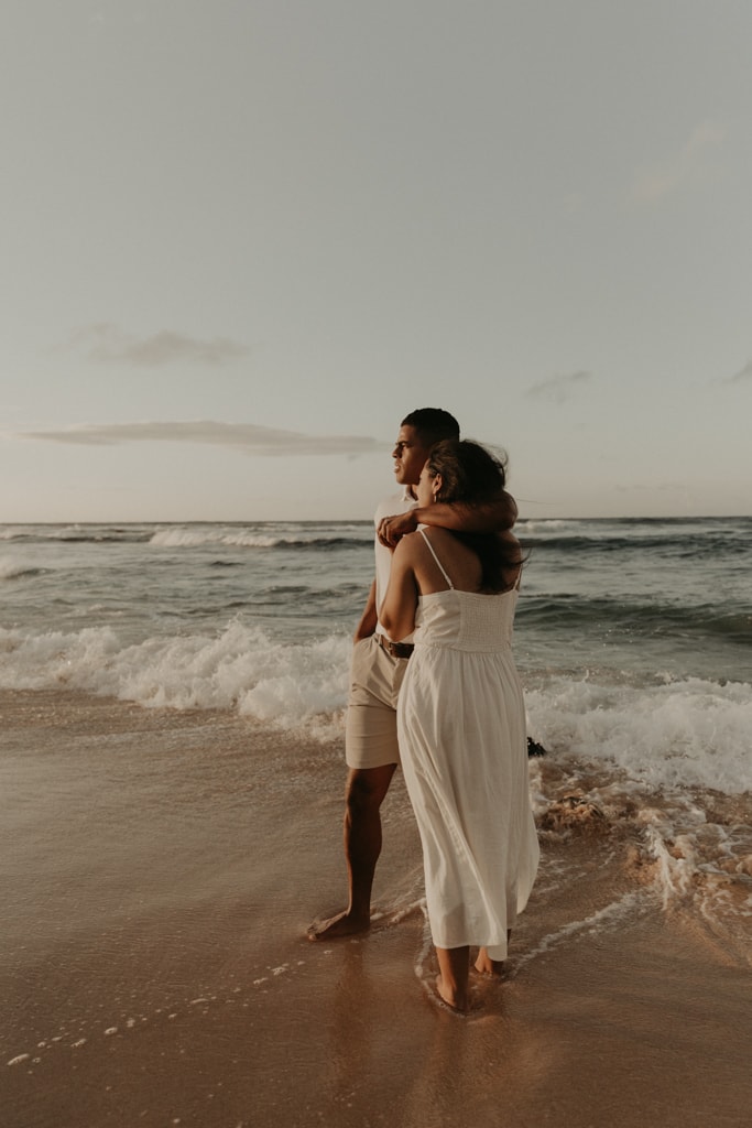 Couple embracing on the beach and looking out to the ocean