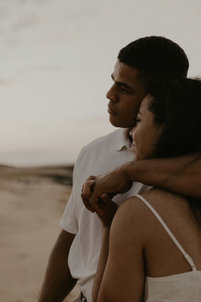 Close up of couple embracing and looking out towards the ocean during sunrise