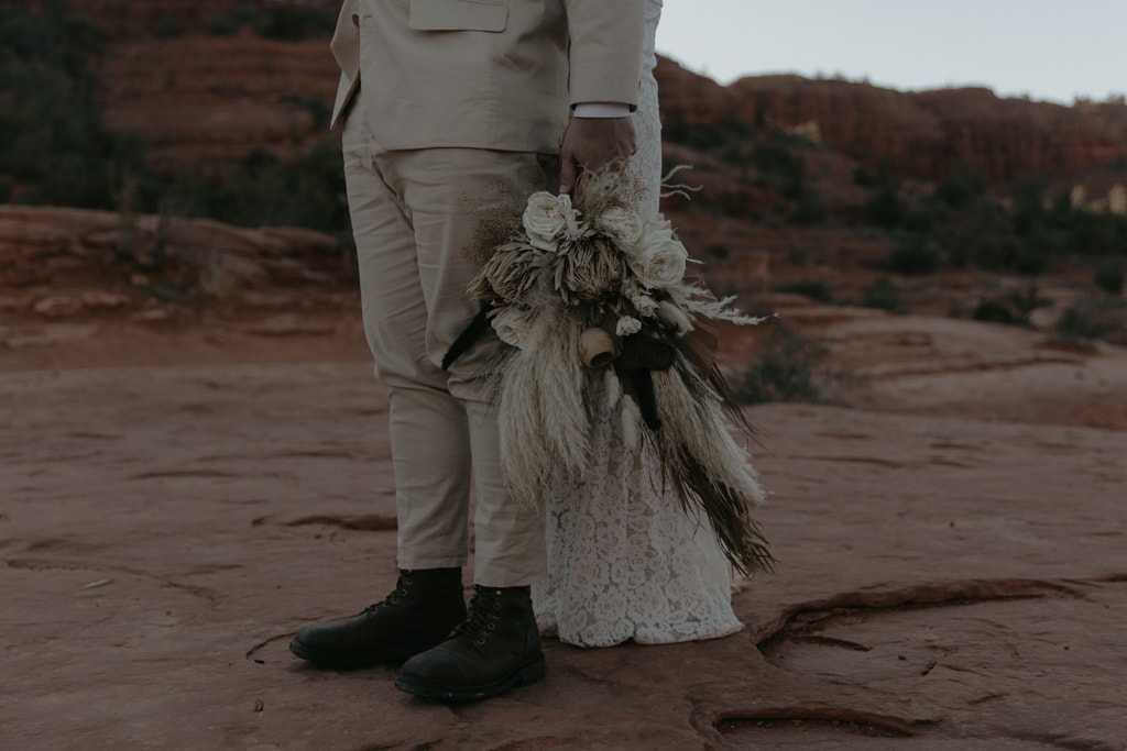 Groom holding bride's flowers in a desert elopement.