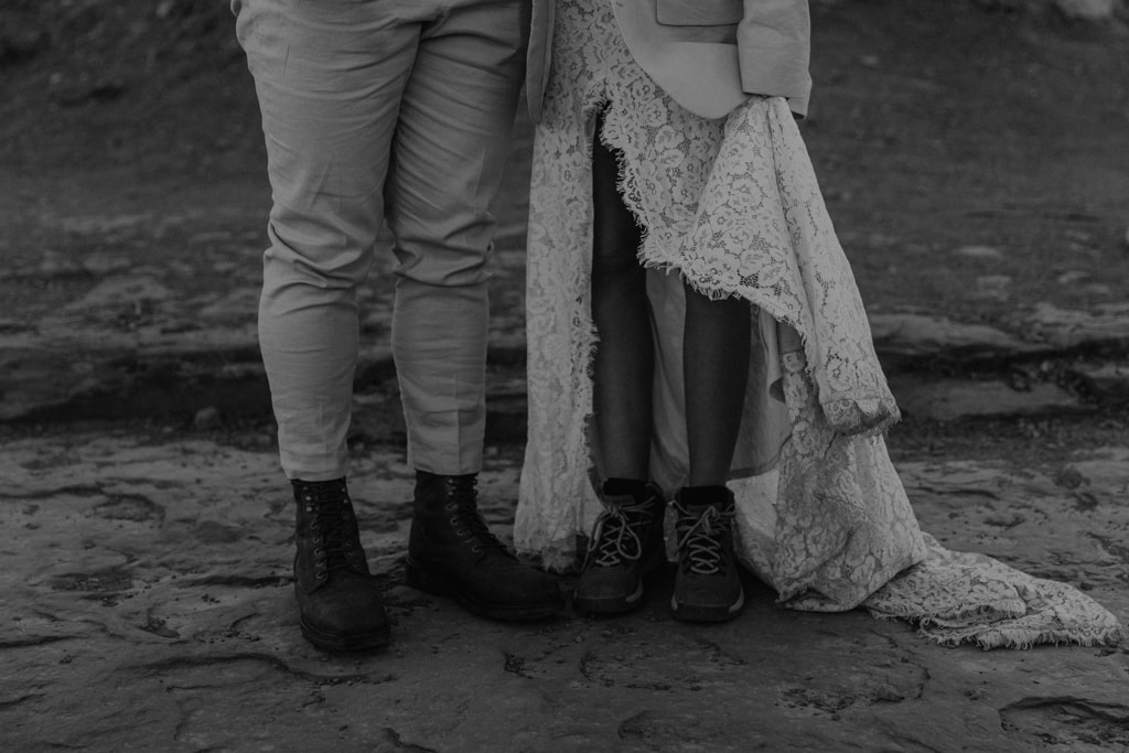 Black and white of adventurous couple with their wedding clothes over hiking boots