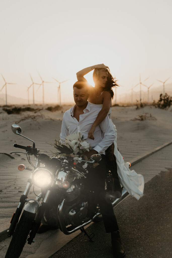 Couple on a motorcycle on a windy elopement day with sun setting behind them