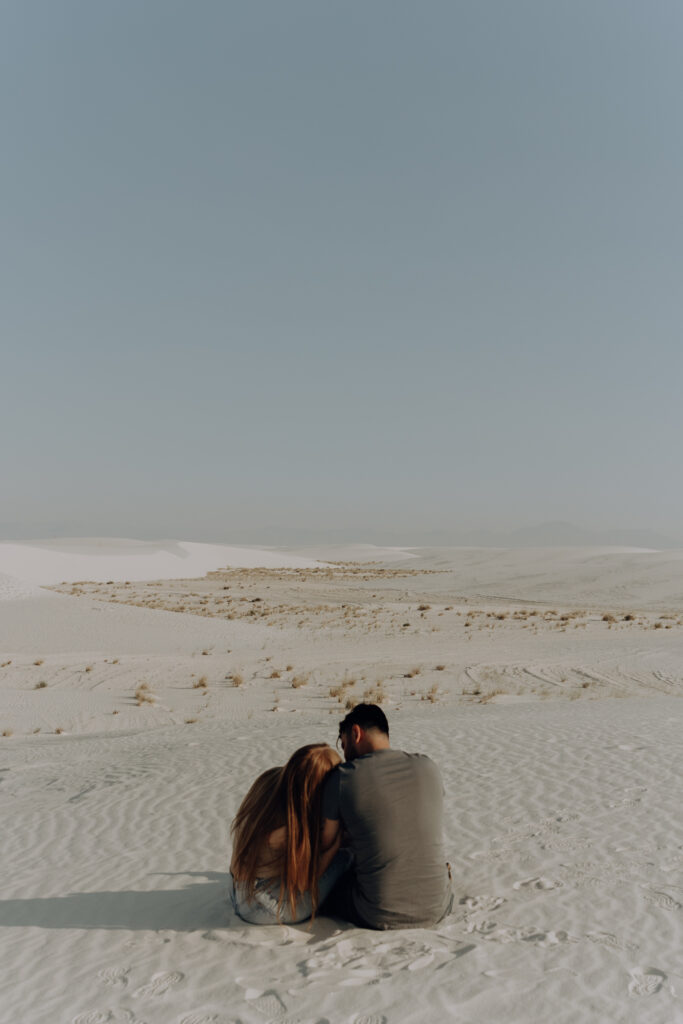 Woman laying her head on man's shoulder looking out over sand dunes.