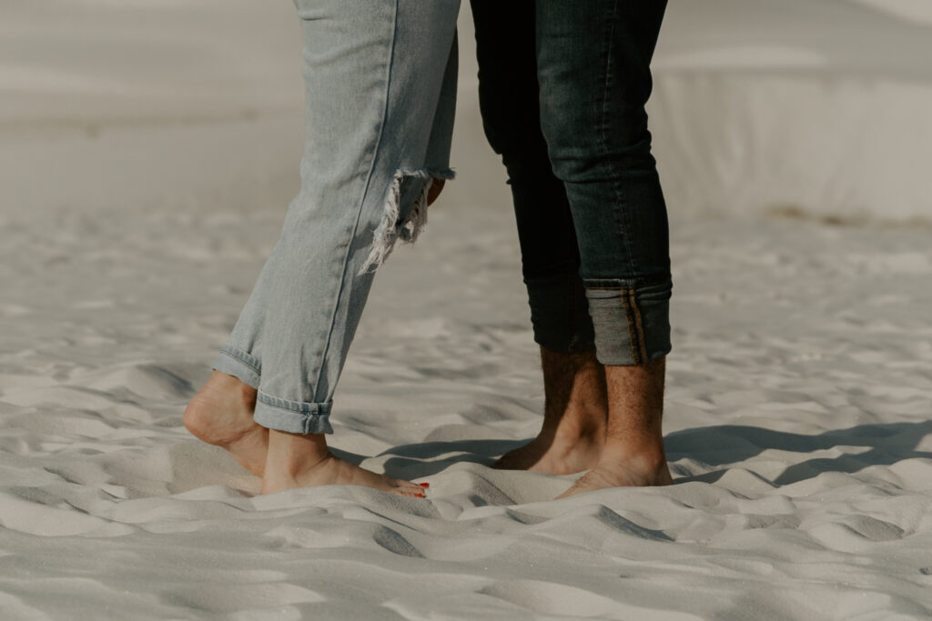 Close up of couple's legs in jeans facing each other in sand