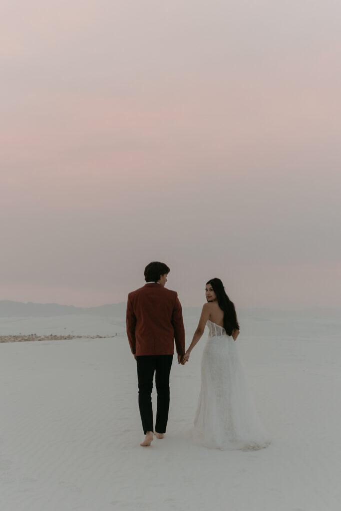 Couple walking towards pink sunset in white sand