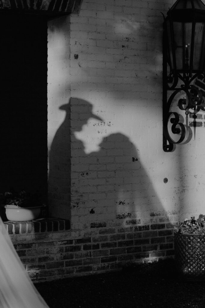 Black and white image of couple's shadows behind them with groom's cowboy hat and bride's veil